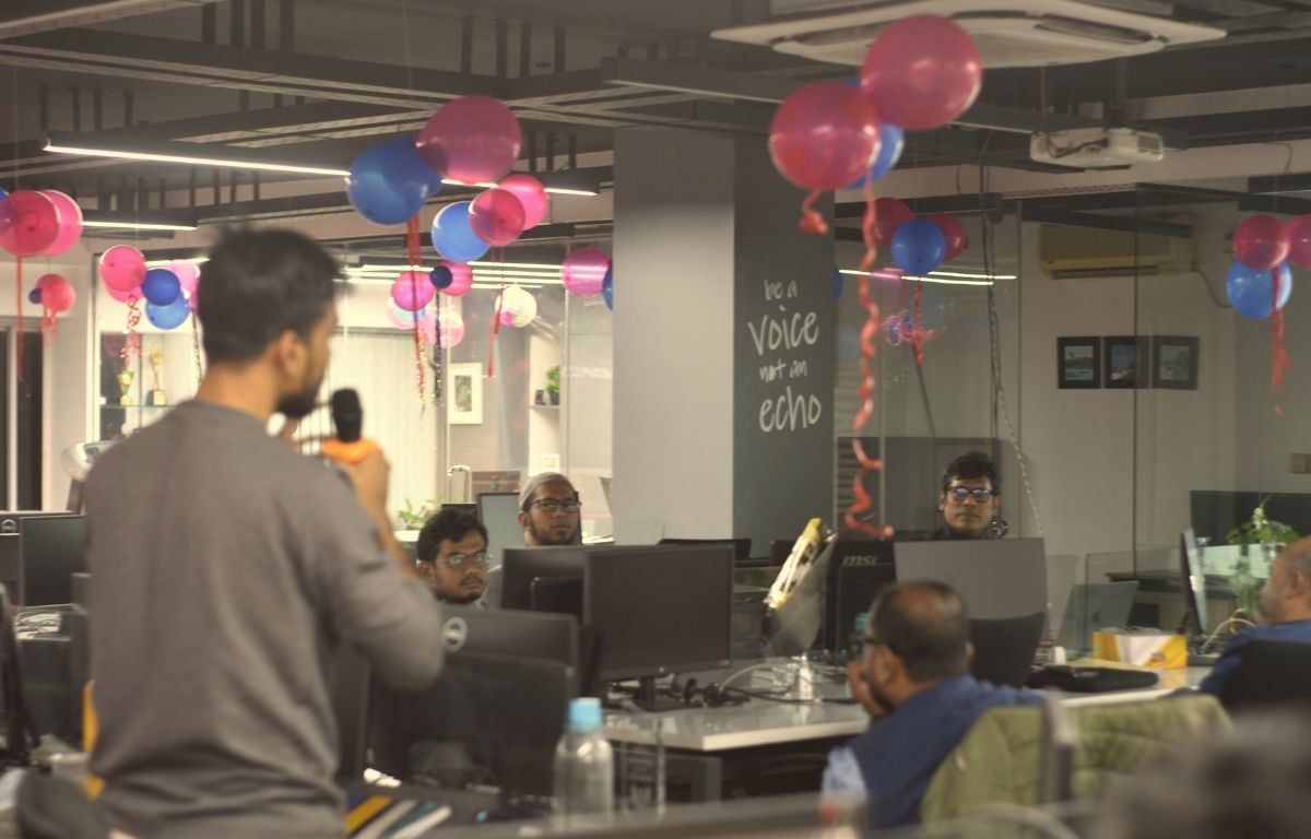 Team discussion inside Ixora Solution office, showing employees collaborating around computers during an internal session, representing organizational communication, shared understanding, and decision-making in a modern workplace.